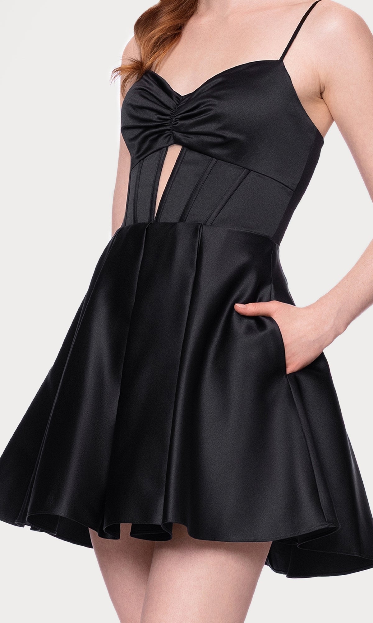 A woman wears the Cut-Out Black Mini Hoco Dress: Blondie Nites 5605BN—an a-line black satin party dress with thin straps, fitted bodice and front cut-out, flared skirt, and side pocket—perfect as a chic homecoming look.
